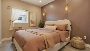 Un dormitorio con cama, mesita de noche, lámpara y ventana con cortinas.