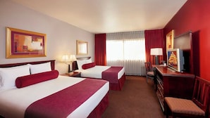 A hotel room with two beds, a desk, a chair, a television, and artwork on the walls.