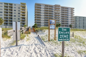 A beachside view of a hotel named "The Enclave" with a sign indicating its address. - The Enclave 301 | Gulf Front Corner Condo | Wraparound Balcony | My Beach Getaways (Orange Beach)