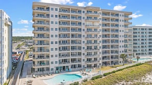 A multi-story hotel with balconies, a swimming pool, and a view of the beach. - The Enclave 301 | Gulf Front Corner Condo | Wraparound Balcony | My Beach Getaways (Orange Beach)