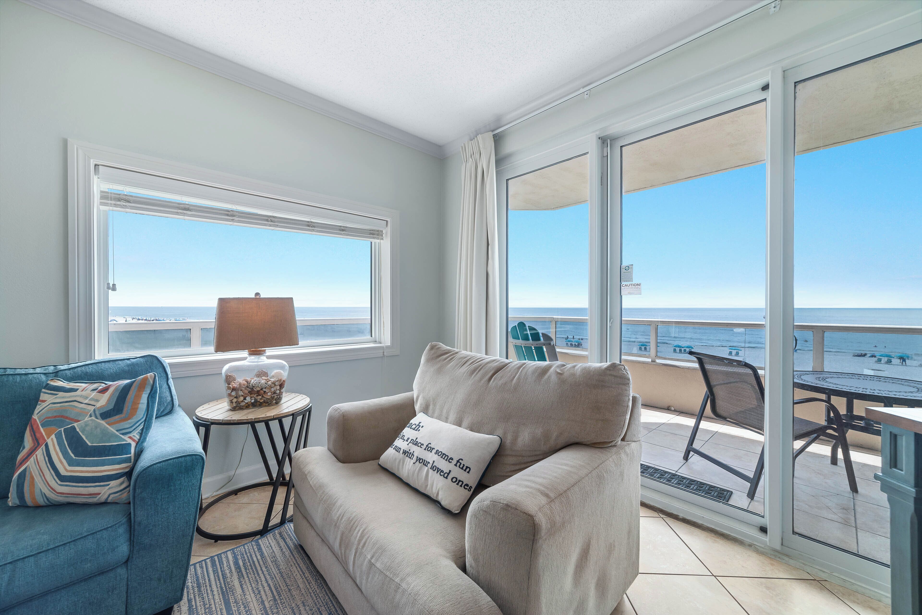 A balcony with a view of the sea, a sofa, a table with a lamp, and a chair.