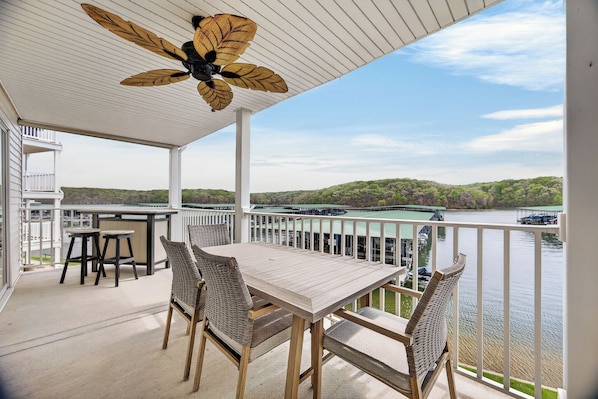 A covered outdoor area with a table and chairs, a ceiling fan, and a view of a lake and dock.