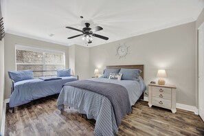 A bedroom with two beds, a ceiling fan, a clock, and a nightstand with a lamp.