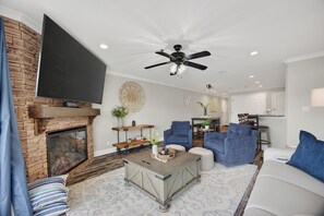 A living room with a fireplace, a ceiling fan, a flat-screen TV, and a dining area with chairs and a table.
