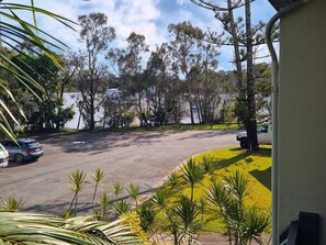 A parking area with cars, a building, and trees in the background. - Noosaville Getaway, Walk to River, Marina and Boat Ramp (Tewantin)
