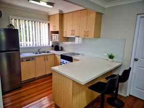 A kitchen with wooden cabinets, a stainless steel refrigerator, a sink, and a small island with two black bar stools. - Noosaville Getaway, Walk to River, Marina and Boat Ramp (Tewantin)