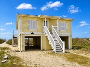 A two-story yellow building with a white staircase, a covered entrance, and a number '125' sign. - Discover 'Diamond in the Rough'—a cozy 3BR oceanfront haven in Oak Island! (Oak Island)