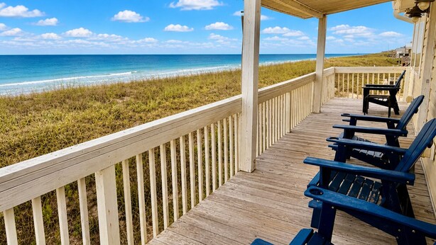 Une terrasse en bois avec des chaises donnant sur une plage.