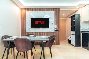 A modern dining area with a flat-screen TV displaying 'NETFLIX,' a marble backsplash, and a wooden accent wall. - Premium Studio-Heart of hivernage, 1 Min to La Gare (Marrakech)