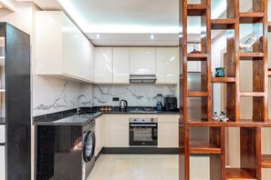 A modern kitchen with a washing machine, oven, and a wooden shelf unit. - Premium Studio-Heart of hivernage, 1 Min to La Gare (Marrakech)