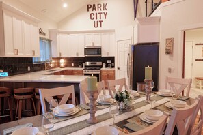 Uma cozinha moderna com armários brancos, uma ilha central e um espaço de jantar preparado para seis pessoas, com a mesa posta para refeição.