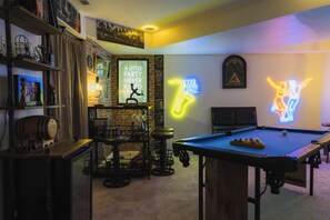 Una mesa de billar, un letrero de neón y una zona de bar con estantes y taburetes.