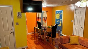 A living room with a sofa, a dining table with chairs, a ceiling fan, and a TV on the wall.
