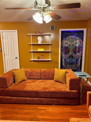 A living room with a sofa, a ceiling fan, a shelf with decorative items, and a patterned curtain. - That 70’s House: boogie woogie bungalow. (Salina)