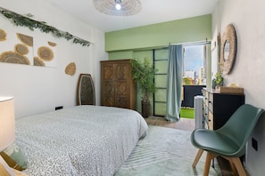 A bedroom with a bed, a chair, a wardrobe, a potted plant, and a view through a window.