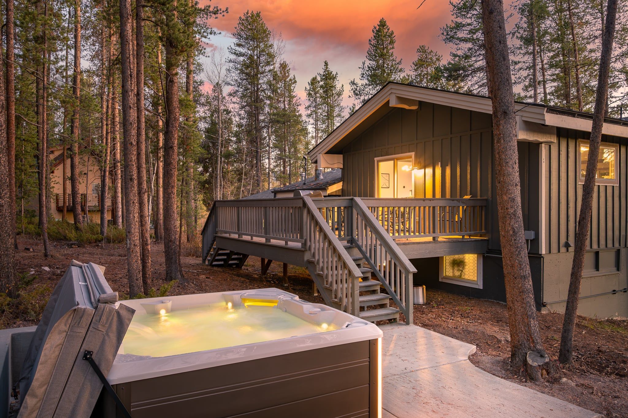 A cabin with a hot tub, wooden deck, and a staircase leading to a deck area.