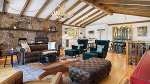 Un vaste espace de vie agrémenté d’une cheminée en pierre, de meubles en cuir et d’un plafond en bois.