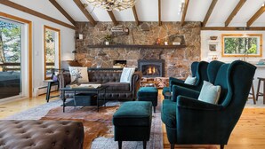 Un salon chaleureux avec une cheminée en pierre, un canapé en cuir, des fauteuils turquoise et un lustre.