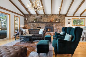 Ein gemütliches Wohnzimmer mit Kamin aus Stein, einer Ledersofa, Türkis-farbenen Sesseln und einer Chandelier.