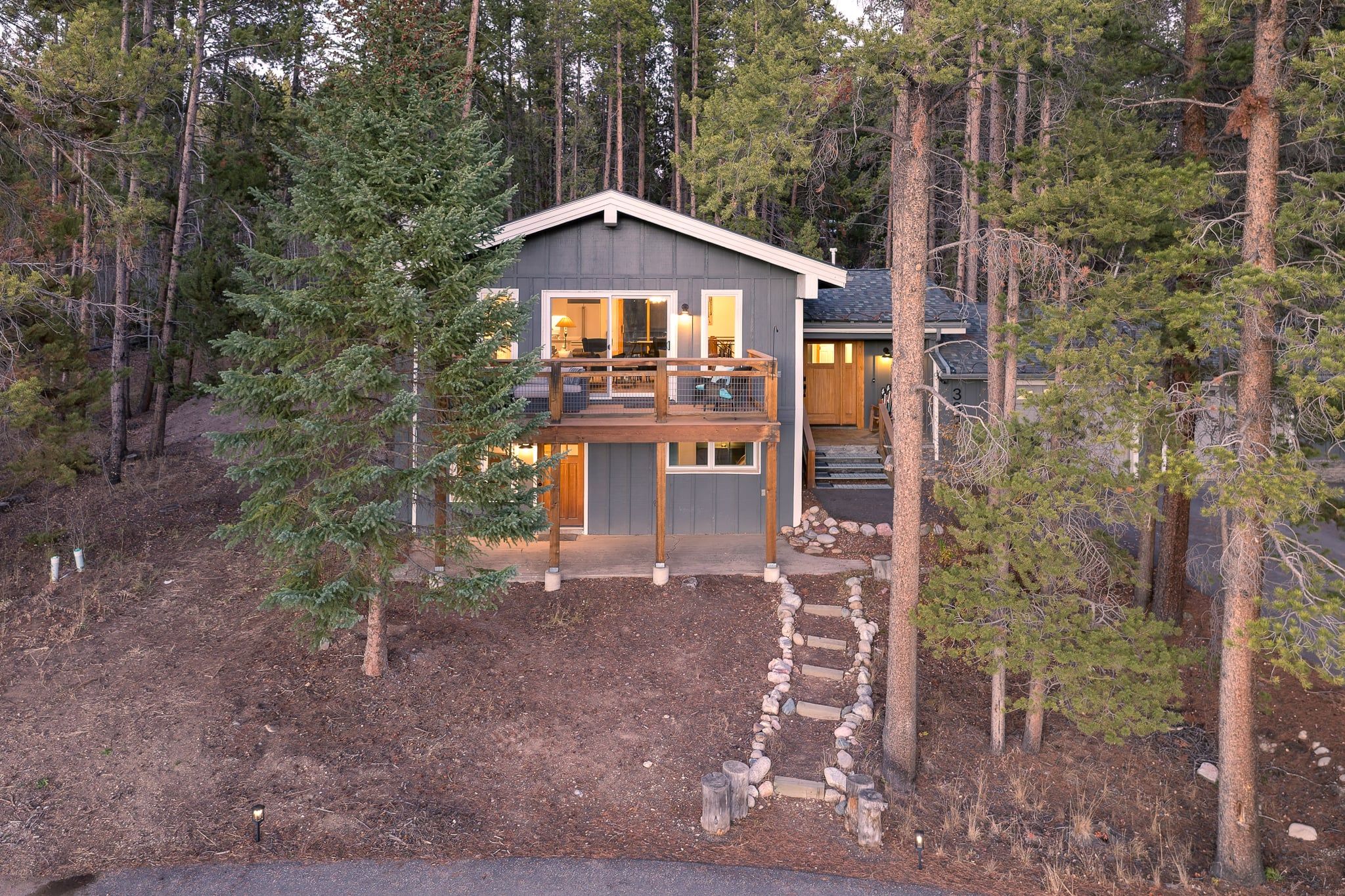 A two-story cabin with a deck, surrounded by trees.