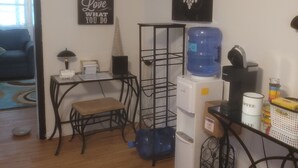 Une petite cuisine bien aménagée, équipée d’un distributeur d’eau, d’une machine à café et d’un panneau affiché sur le mur.
