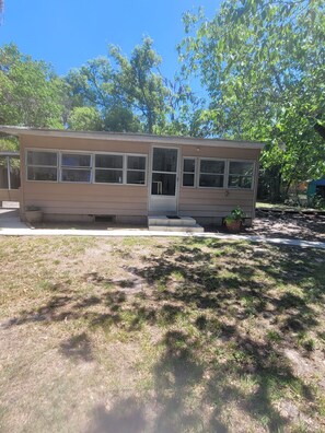 A single-story mobile home with a front porch, a small garden area, and a clear sky.