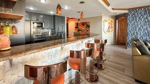 A modern kitchen with a marble countertop, stainless steel appliances, and a bar area with stools. - The Iconic Beachfront 3BR Condo (Puerto Peñasco)