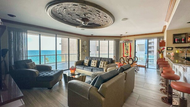 A spacious living area with a large sofa, a coffee table, and a bar with stools. - The Iconic Beachfront 3BR Condo (Puerto Peñasco)