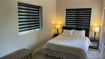 A bedroom with a bed, two bedside lamps, a nightstand, a wooden bench, and a window with blinds.