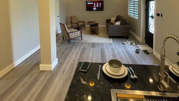A modern living room with a flat-screen TV, a sofa, and a dining area with a marble countertop and a sink. - Church street Apartments  (Georgetown)