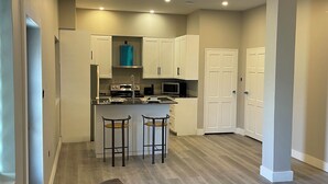 A modern kitchen with white cabinets, a central island with stools, and a built-in microwave. - Church street Apartments  (Georgetown)