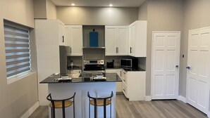 A modern kitchen with white cabinets, a central island with stools, and a microwave. - Church street Apartments  (Georgetown)