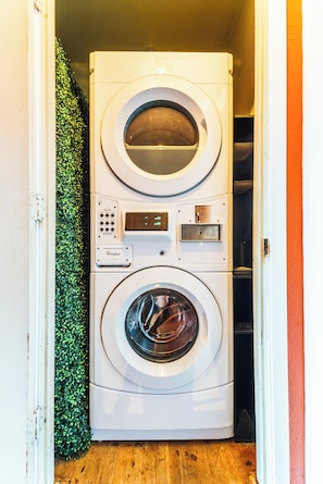 Un appareil combiné lave-linge et sèche-linge, avec un panneau de commande, installé dans un couloir étroit doté d’un plancher en bois et d’un mur vert.