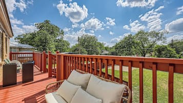 A wooden deck with a red railing, a wicker sofa with cushions, and a trash can.