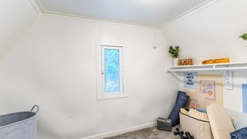 A room with a sloped ceiling, a window with a view, a shelf with decorative items, and a storage unit with exercise equipment.