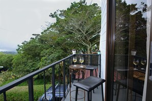 A balcony with two tables, each with a glass of wine, overlooking a lush green landscape. - Alma Verde (Monteverde)