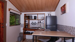 Eine kleine Küche mit Mikrowelle, Wasserkocher und Kühlschrank. Ein Holztisch und zwei Stühle stehen bereit.