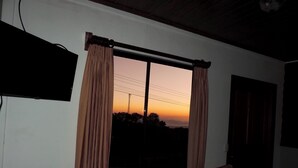 Ein Zimmer mit Fenster, Vorhängen, Fernseher und Stuhl.
