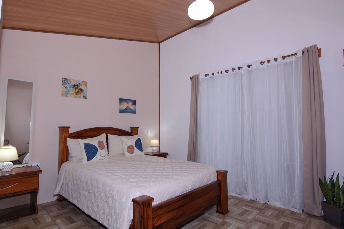 A bedroom with a wooden bed, bedside tables, a mirror, and a potted plant.
