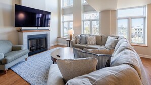 Una sala de estar con chimenea, un televisor de pantalla plana grande, un sofá seccional y una mesa de centro.