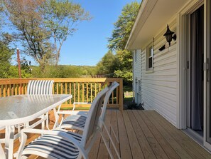 A wooden deck with a table and chairs, a railing, and a house with a window and a door. - Charming 2-bedroom house with AC in Wolcott perfect for relaxing (Wolcott)