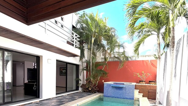 Piscina com deck de madeira, parede vermelha e palmeiras.