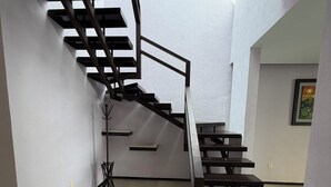Uma escada moderna com guarda-corpo de metal, uma pequena mesa e uma cadeira em um quarto claro e com paredes brancas.