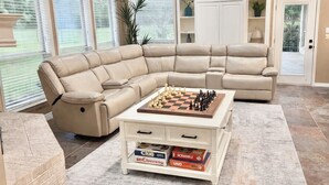A living room with a sectional sofa, a coffee table with chess and board games, and a brick accent wall.