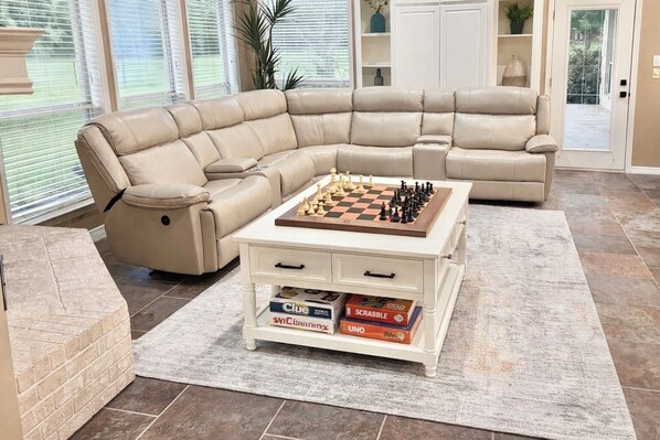 Un salon avec un canapé d’angle, une table basse sur laquelle on trouve un jeu d’échecs et d’autres jeux de société, et un mur décoratif en briques.