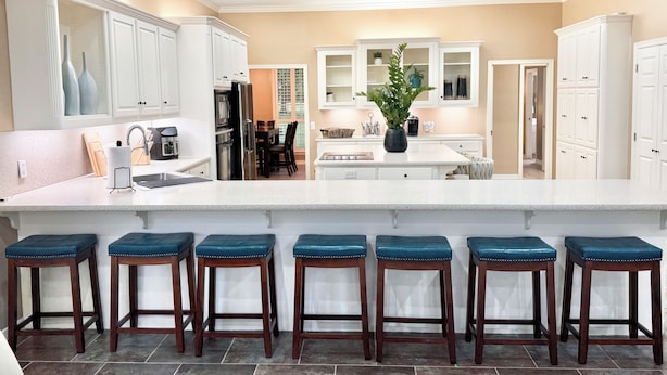 A kitchen with white cabinets, a central island with stools, and a dining area with chairs.