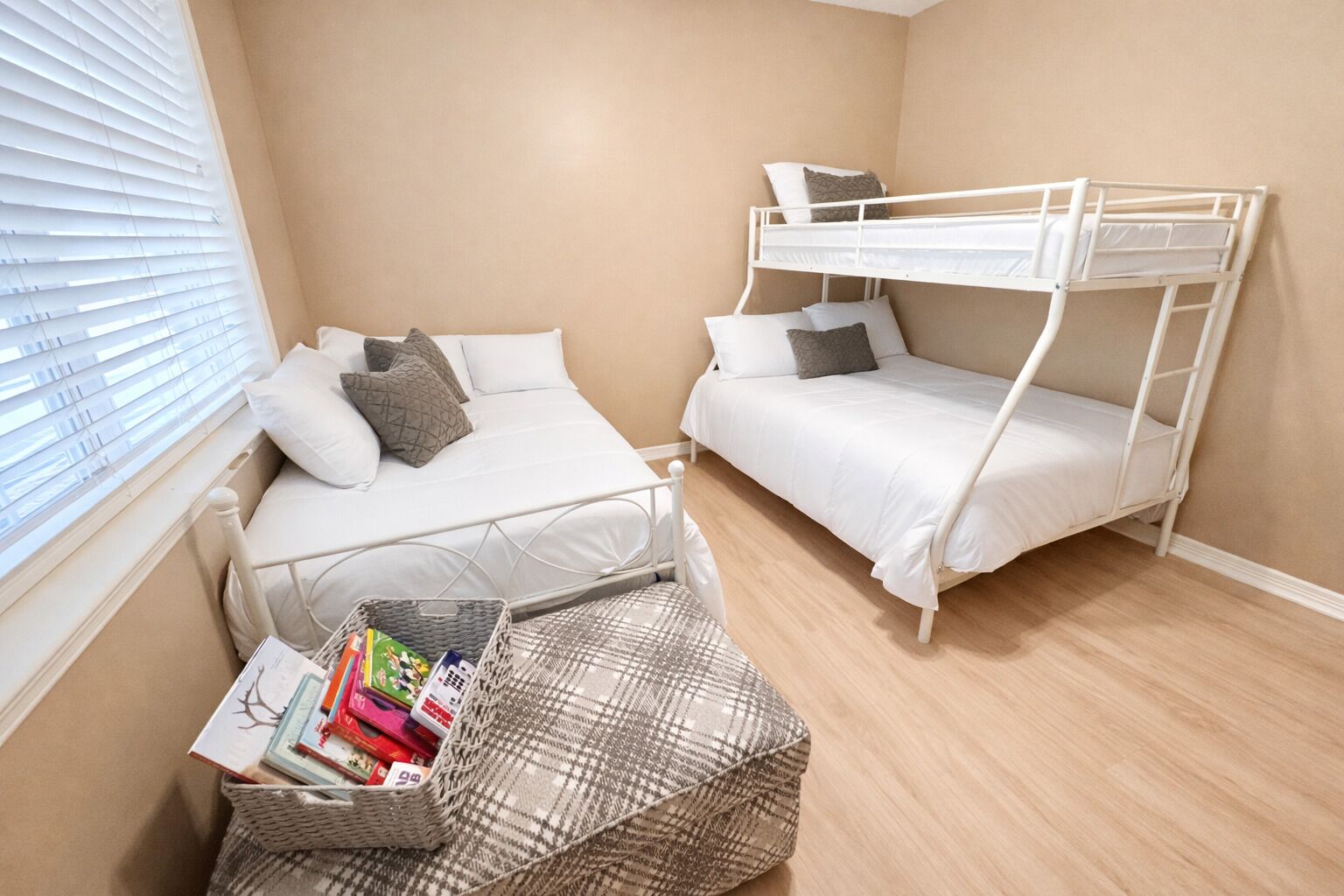 A room with two bunk beds, a window with blinds, a wicker basket with books, and a patterned rug.