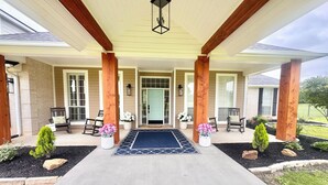 A covered porch with a bench, potted plants, and a door.