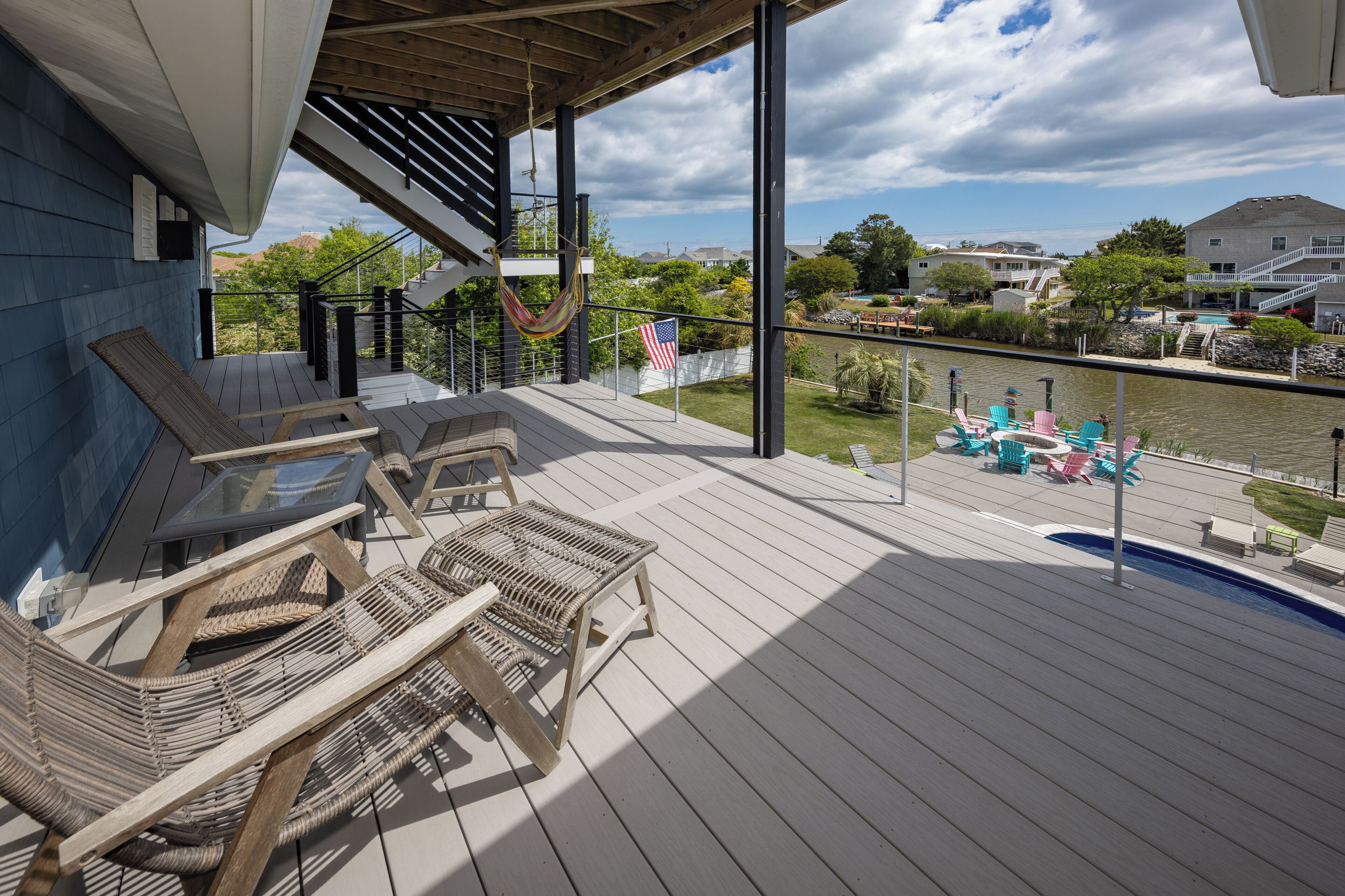 Een houten terras met wickerstoelen en een hangmat, met uitzicht op een waterpartij met boten en huizen op de achtergrond.
