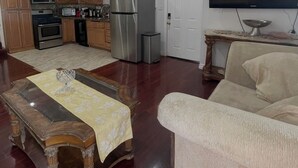 Un soggiorno con un tavolino in legno, una poltrona, una televisione e una cucina con elettrodomestici.